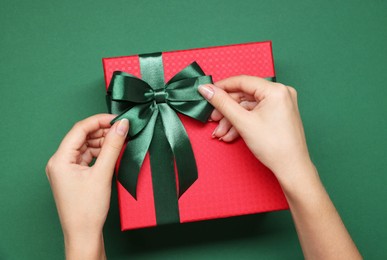 Woman decorating gift box with bow on green background, top view