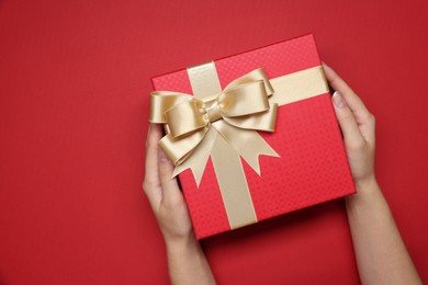 Photo of Woman holding gift box with bow on red background, top view