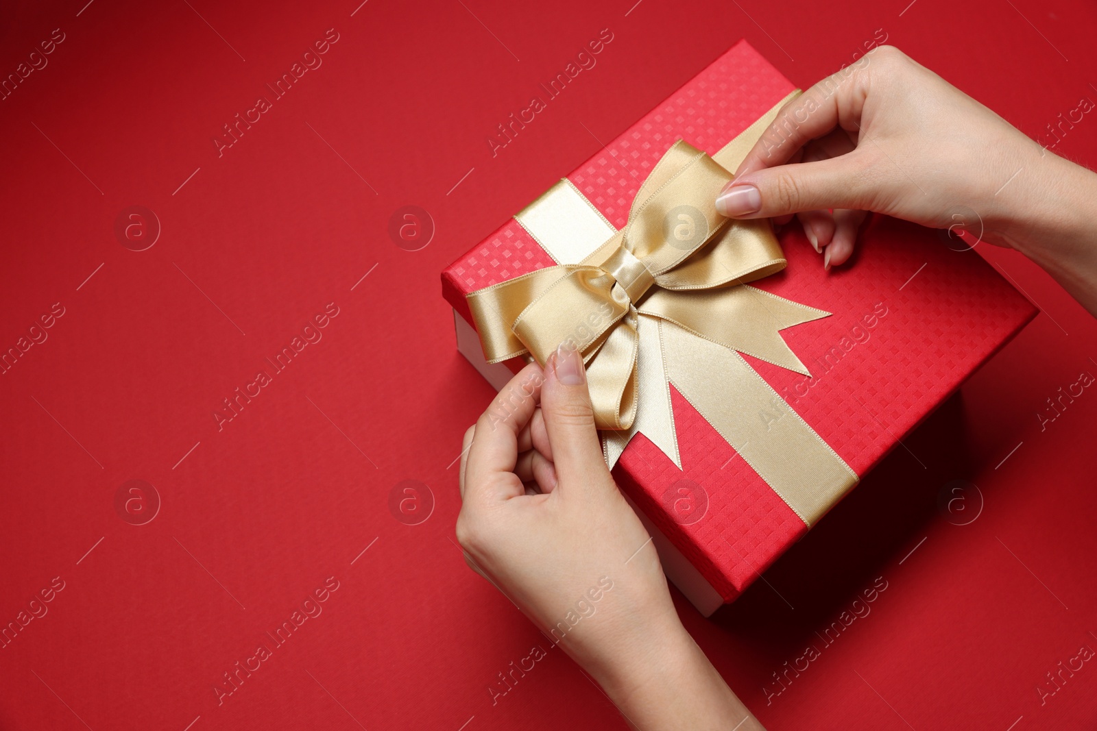 Photo of Woman decorating gift box with bow on red background, closeup. Space for text