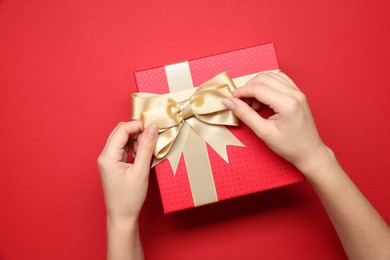 Photo of Woman decorating gift box with bow on red background, top view