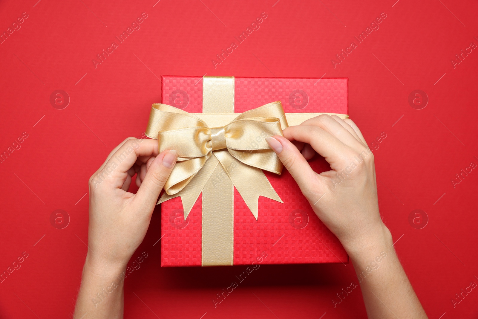 Photo of Woman decorating gift box with bow on red background, top view