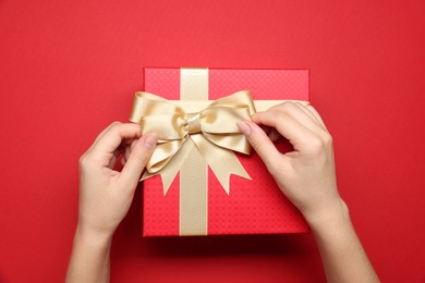 Photo of Woman decorating gift box with bow on red background, top view