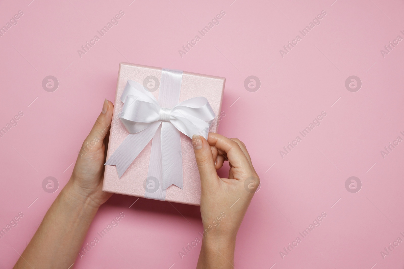 Photo of Woman decorating gift box with bow on pink background, top view. Space for text