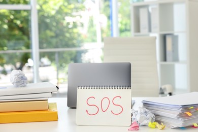 Photo of Notebook with word SOS, stationery and laptop on table in office