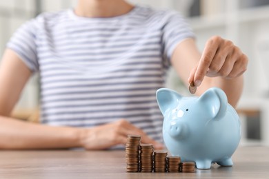 Photo of Woman putting coin into piggy bank at wooden table, closeup