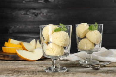 Photo of Scoops of melon sorbet in glass dessert bowls and spoons on wooden table