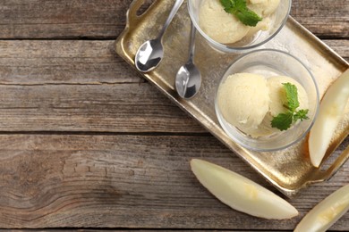 Photo of Scoops of melon sorbet with mint in glass dessert bowls, fresh fruit and spoons on wooden table, flat lay. Space for text