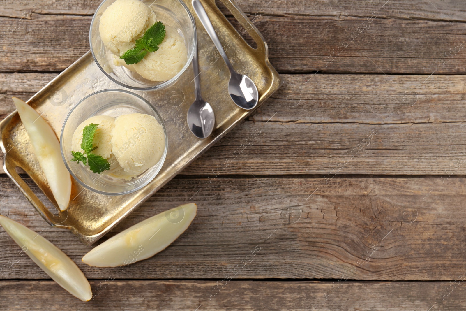 Photo of Scoops of melon sorbet with mint in glass dessert bowls, fresh fruit and spoons on wooden table, flat lay. Space for text