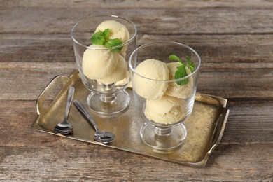 Photo of Scoops of melon sorbet with mint in glass dessert bowls, fresh fruit and spoons on wooden table