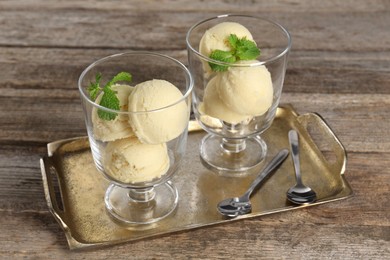 Photo of Scoops of melon sorbet with mint in glass dessert bowls, fresh fruit and spoons on wooden table