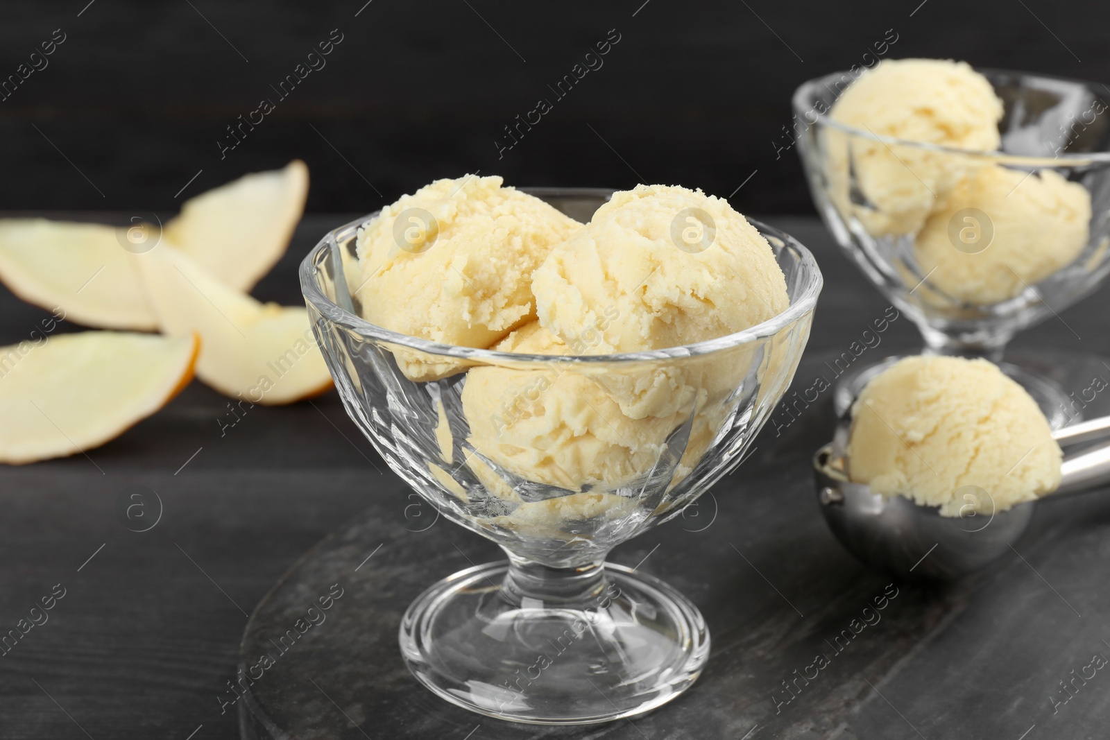 Photo of Scoops of melon sorbet in glass dessert bowls on dark wooden table, closeup