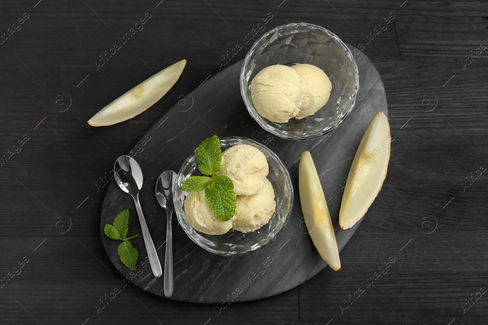 Photo of Scoops of melon sorbet with mint in glass dessert bowls, fresh fruit and spoons on dark wooden table, flat lay