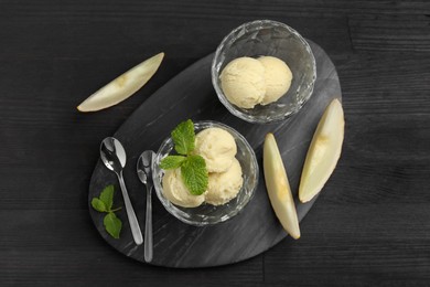 Scoops of melon sorbet with mint in glass dessert bowls, fresh fruit and spoons on dark wooden table, flat lay