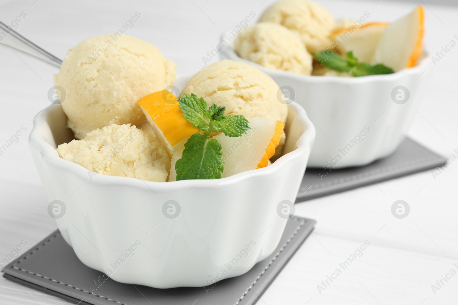 Photo of Scoops of melon sorbet with mint and fresh fruit in bowls on white wooden table, closeup