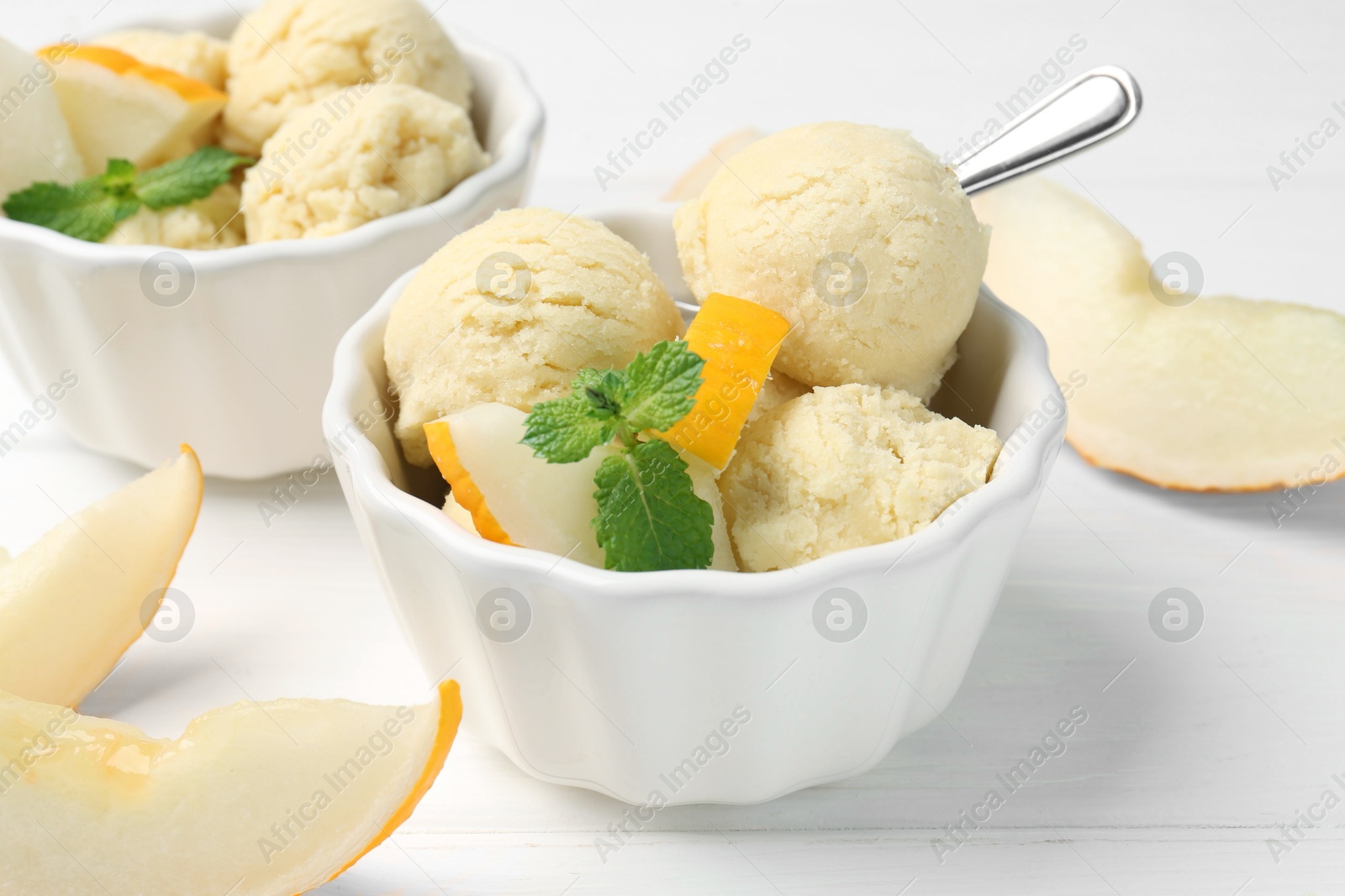 Photo of Scoops of melon sorbet with mint and fresh fruit in bowls on white wooden table, closeup