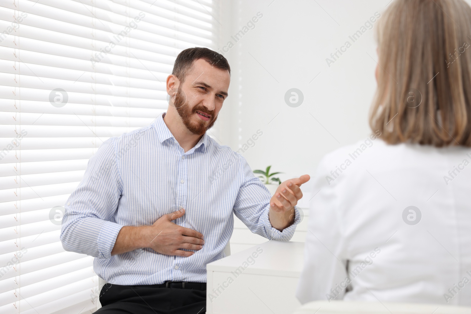 Photo of Doctor consulting patient with stomach pain at table in clinic, back view