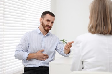 Doctor consulting patient with stomach pain at table in clinic, back view