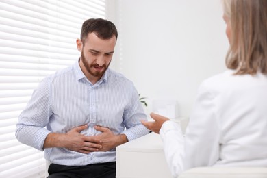 Photo of Doctor consulting patient with stomach pain at table in clinic, back view