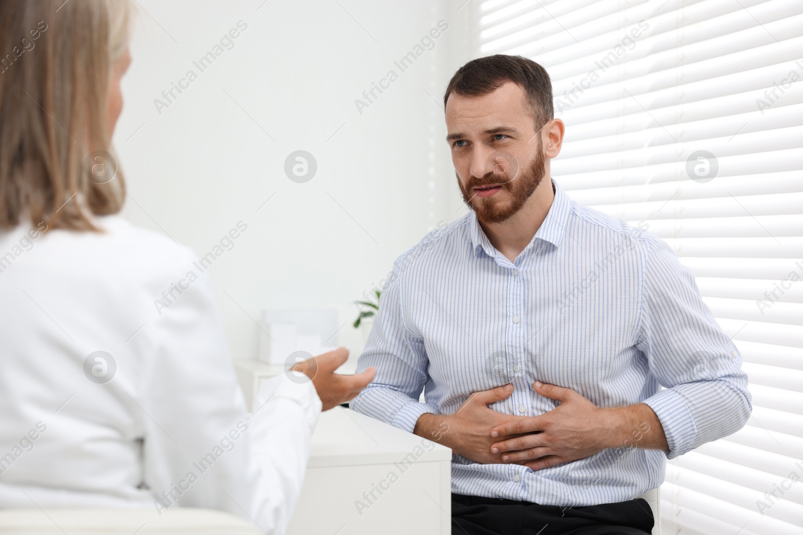 Photo of Doctor consulting patient with stomach pain at table in clinic, back view