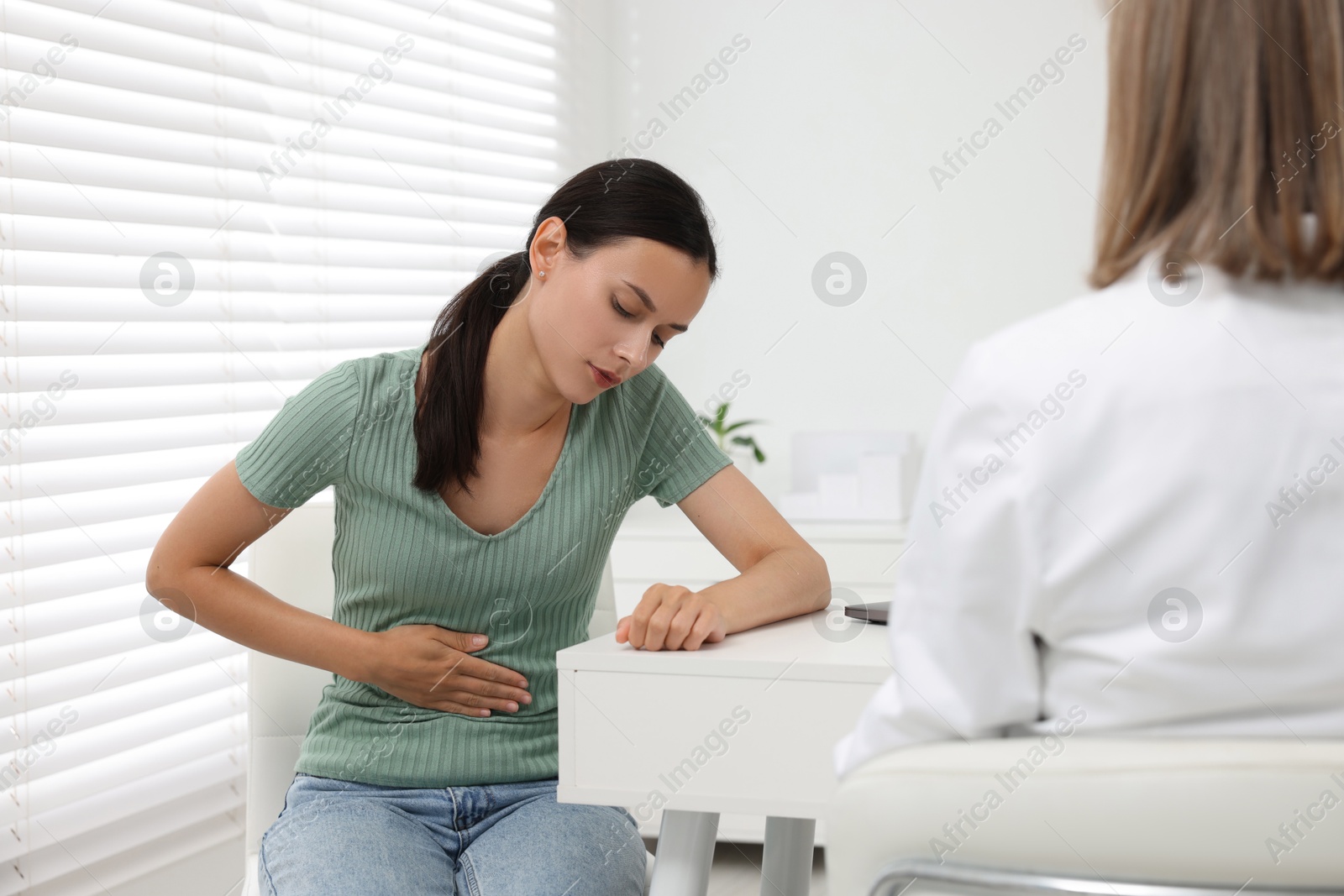 Photo of Doctor consulting patient with stomach pain at table in clinic, back view