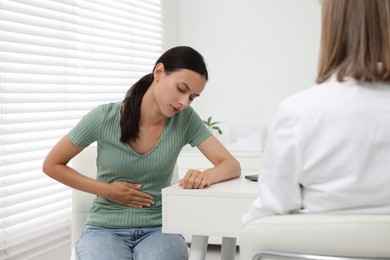 Doctor consulting patient with stomach pain at table in clinic, back view