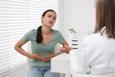 Doctor consulting patient with stomach pain at table in clinic, back view