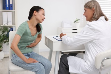 Photo of Doctor consulting patient with stomach pain at table in hospital