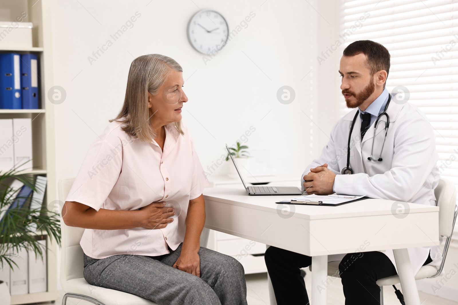 Photo of Doctor consulting senior patient with stomach pain at table in clinic