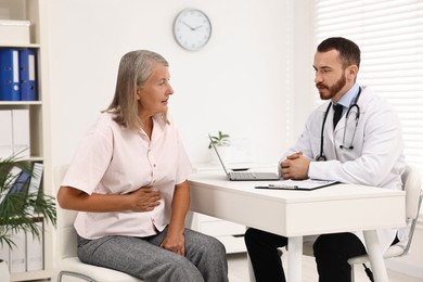 Photo of Doctor consulting senior patient with stomach pain at table in clinic