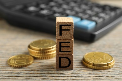 Photo of Cubes with letters Fed (Federal Reserve System) and coins on wooden table, closeup