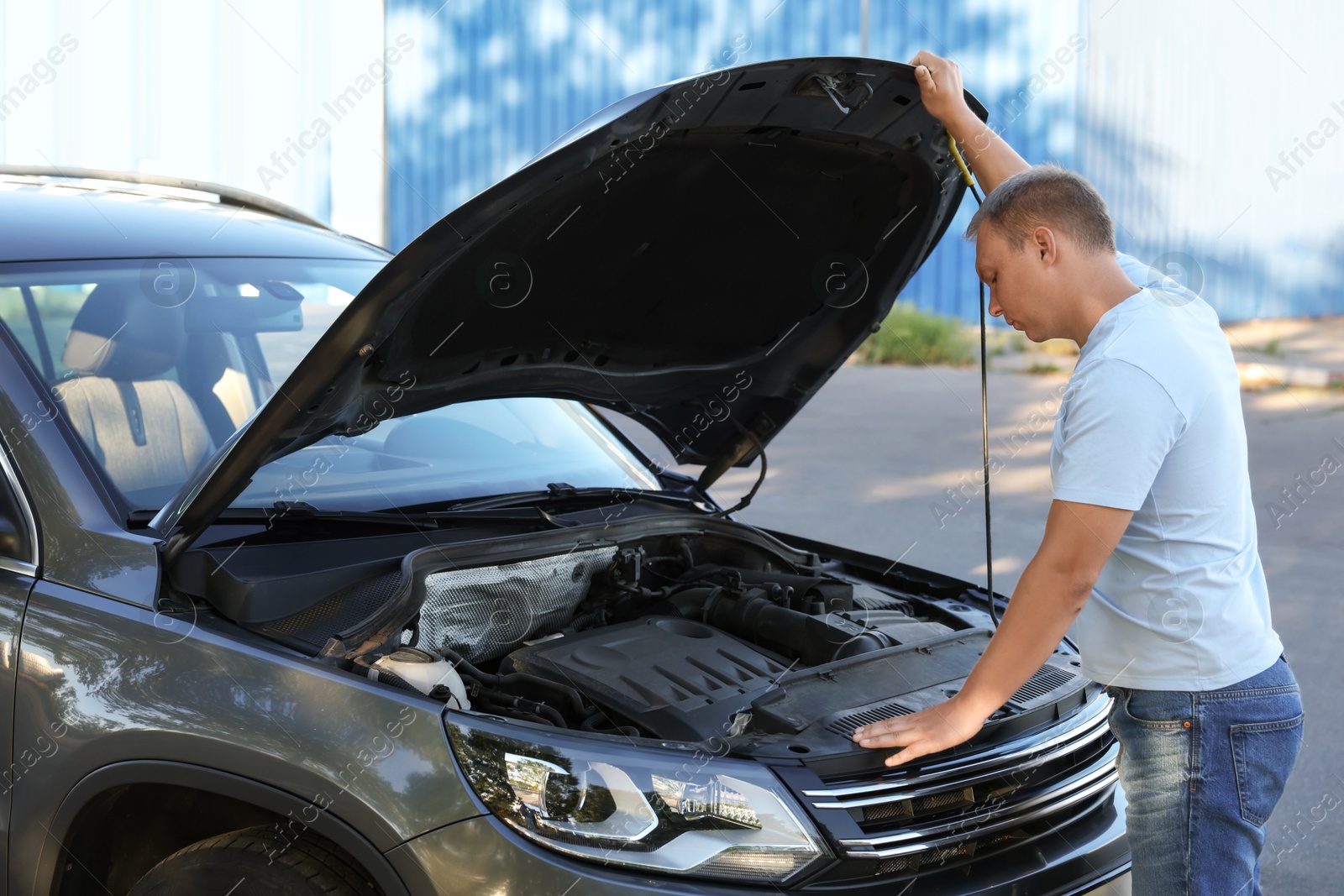 Photo of Stressed man looking under hood of broken car outdoors