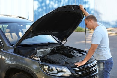 Photo of Stressed man looking under hood of broken car outdoors