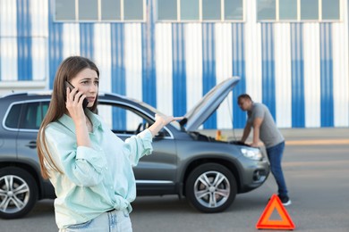 Photo of Man standing near broken auto while woman calling to car service outdoors