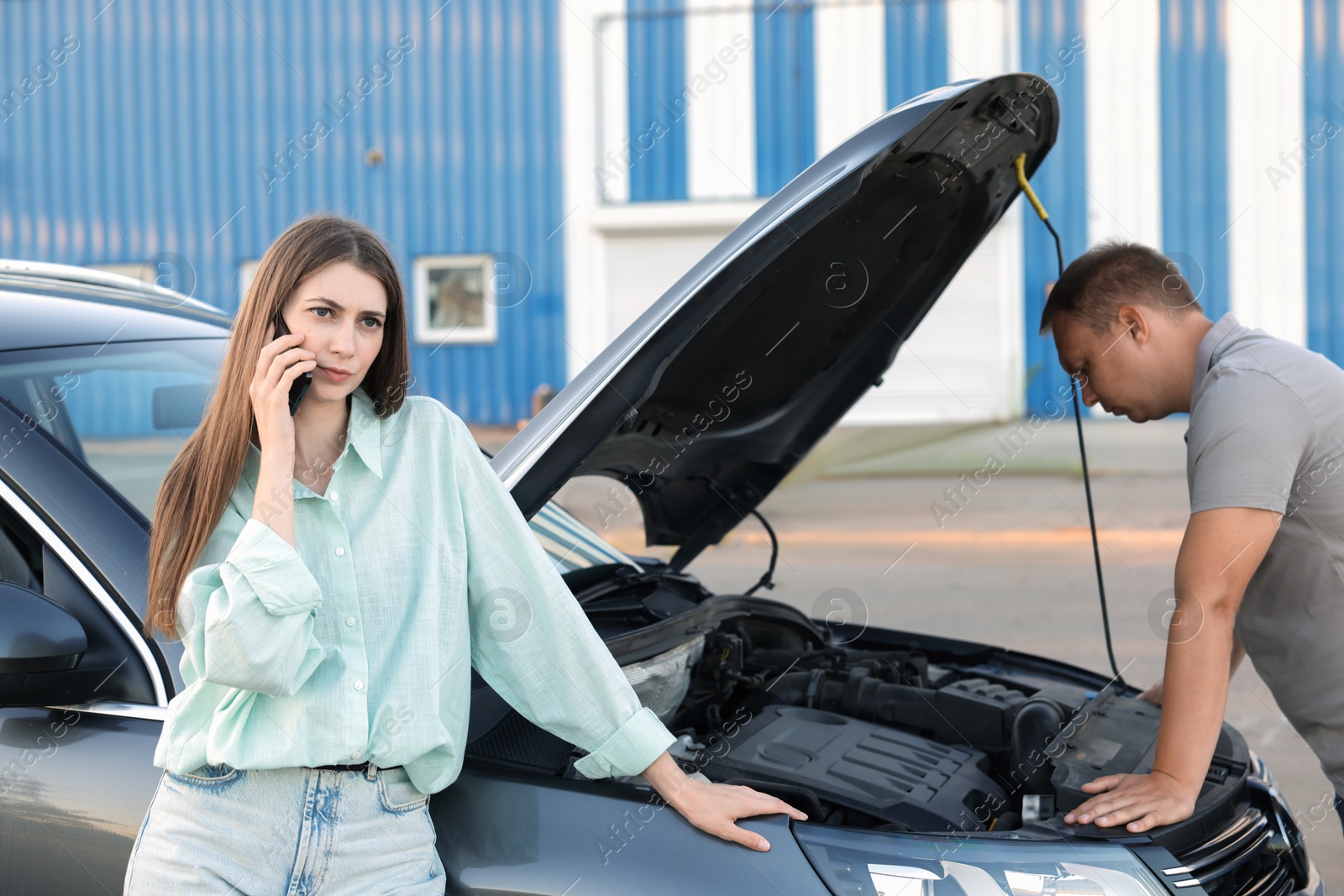 Photo of Man examining broken auto while woman calling to car service outdoors