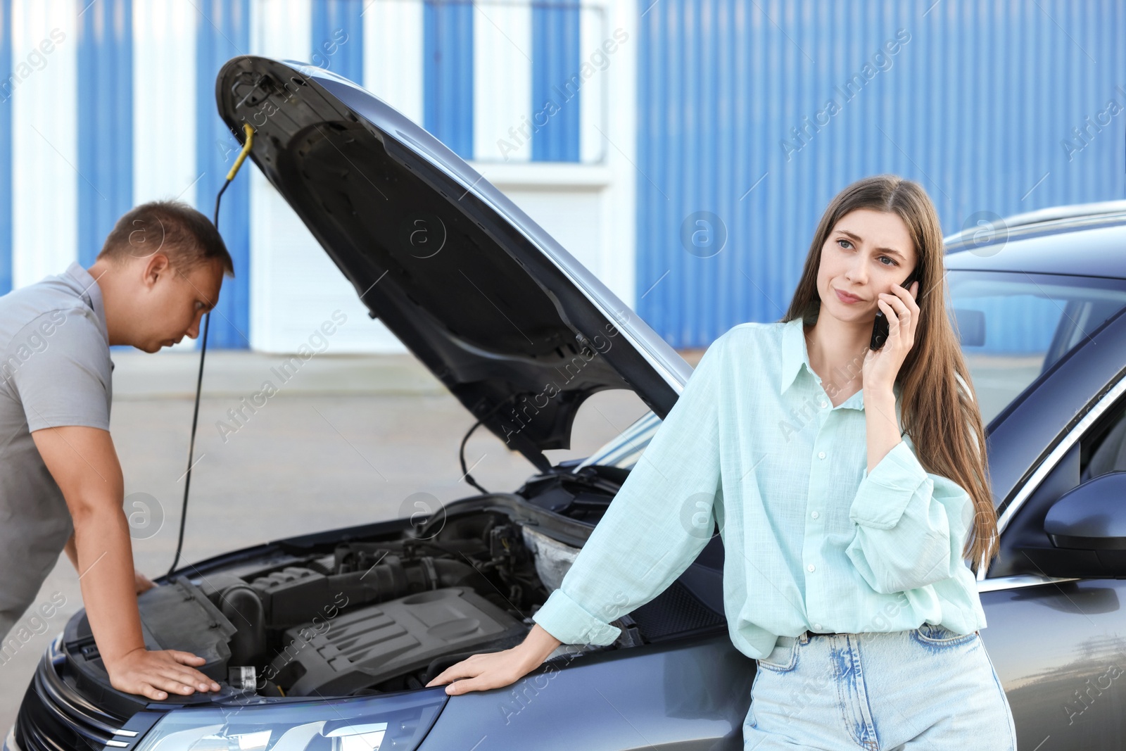 Photo of Man examining broken auto while woman calling to car service outdoors