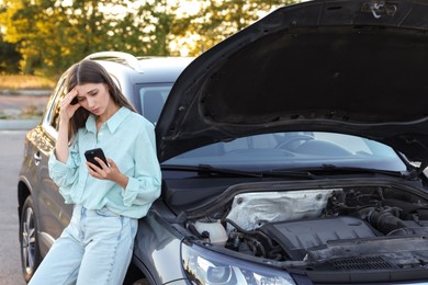 Photo of Stressed woman using smartphone near broken car outdoors