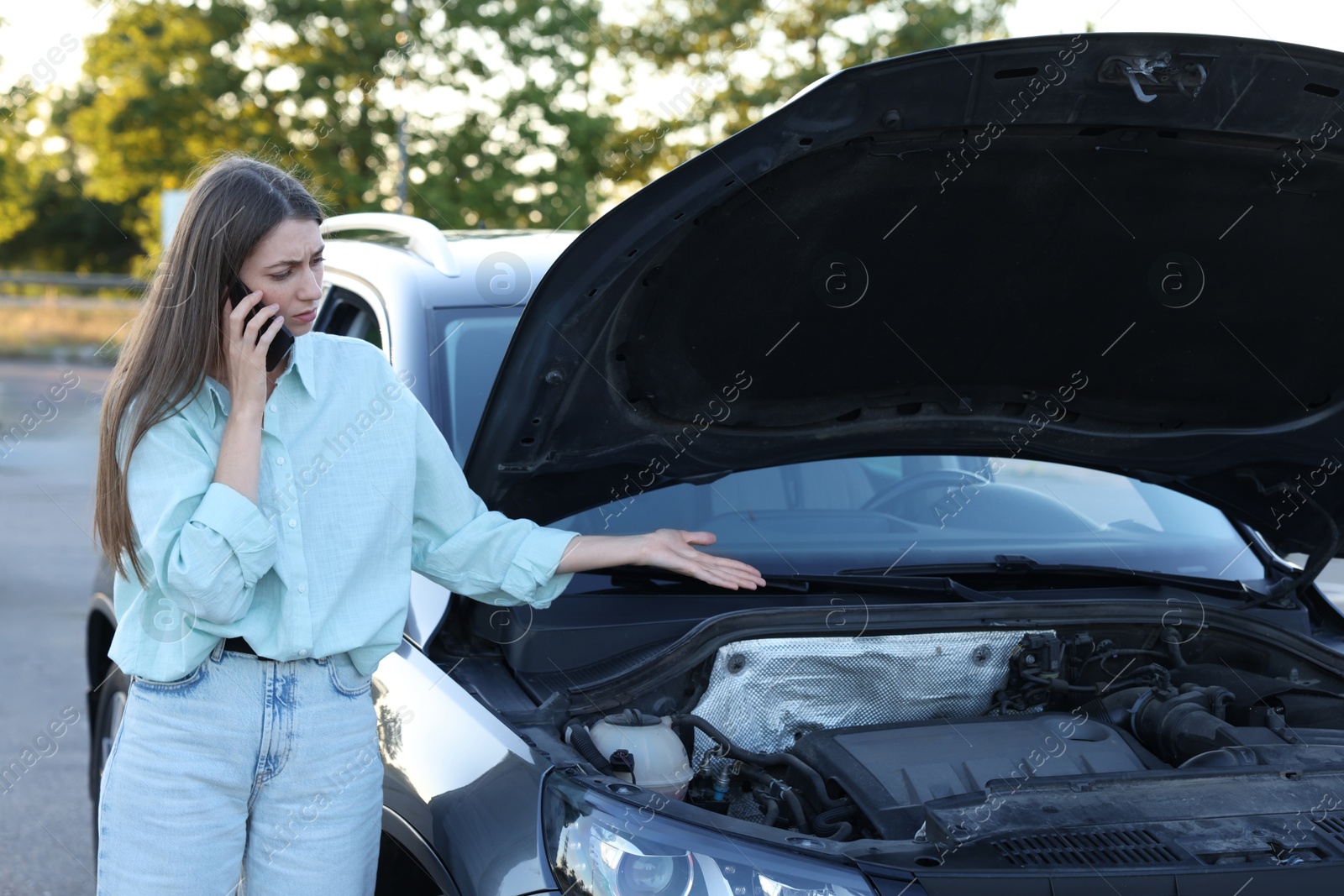 Photo of Stressed woman talking on phone near broken car outdoors