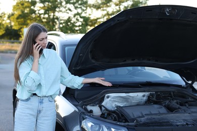 Stressed woman talking on phone near broken car outdoors