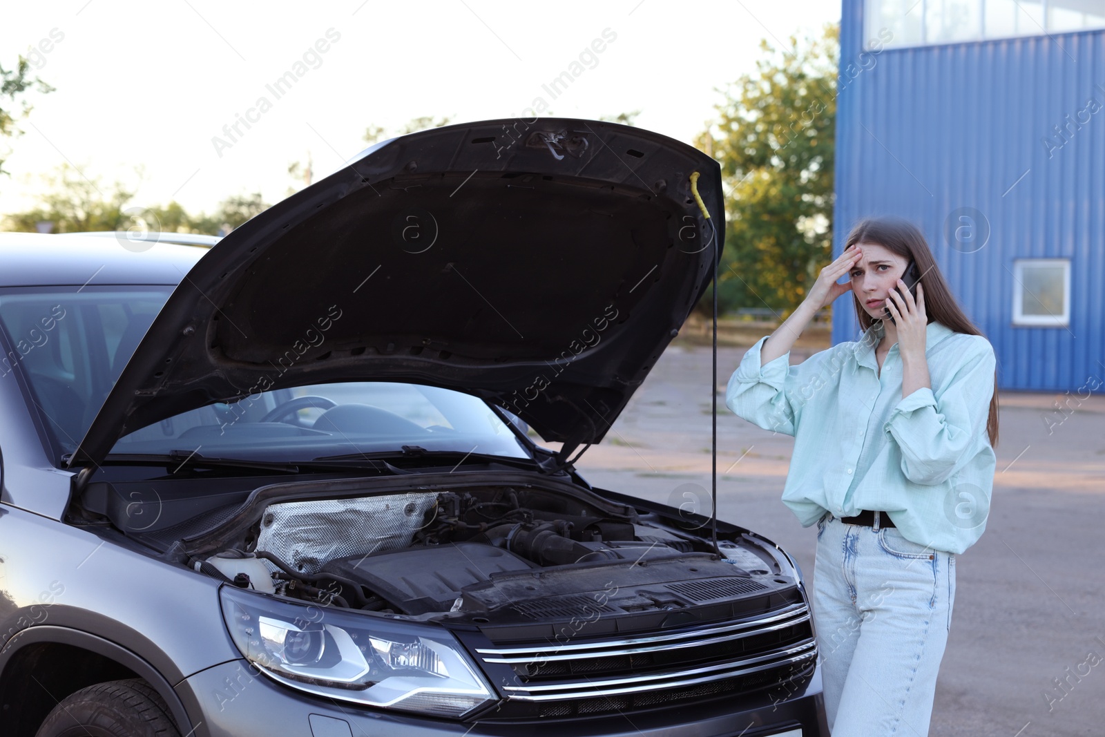 Photo of Stressed woman talking on phone near broken car outdoors