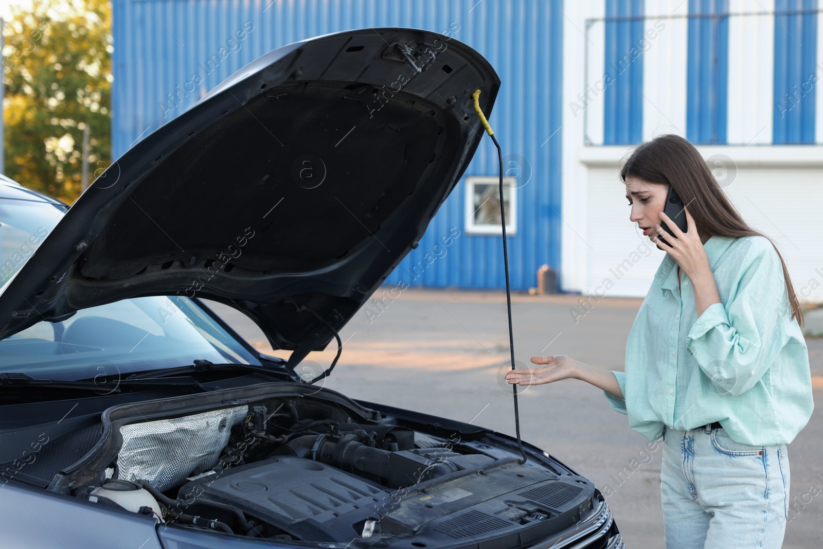 Photo of Stressed woman talking on phone near broken car outdoors