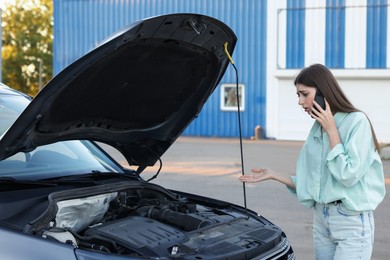 Photo of Stressed woman talking on phone near broken car outdoors