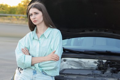 Stressed woman standing near broken car outdoors