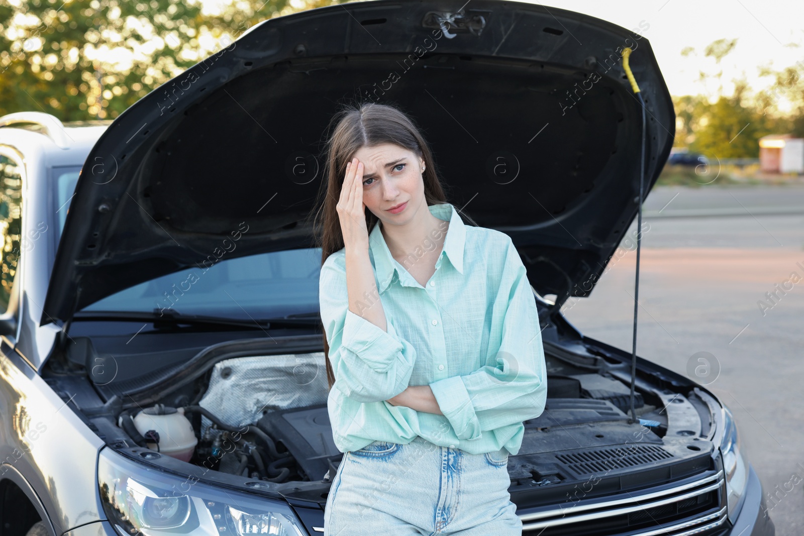 Photo of Stressed woman standing near broken car outdoors