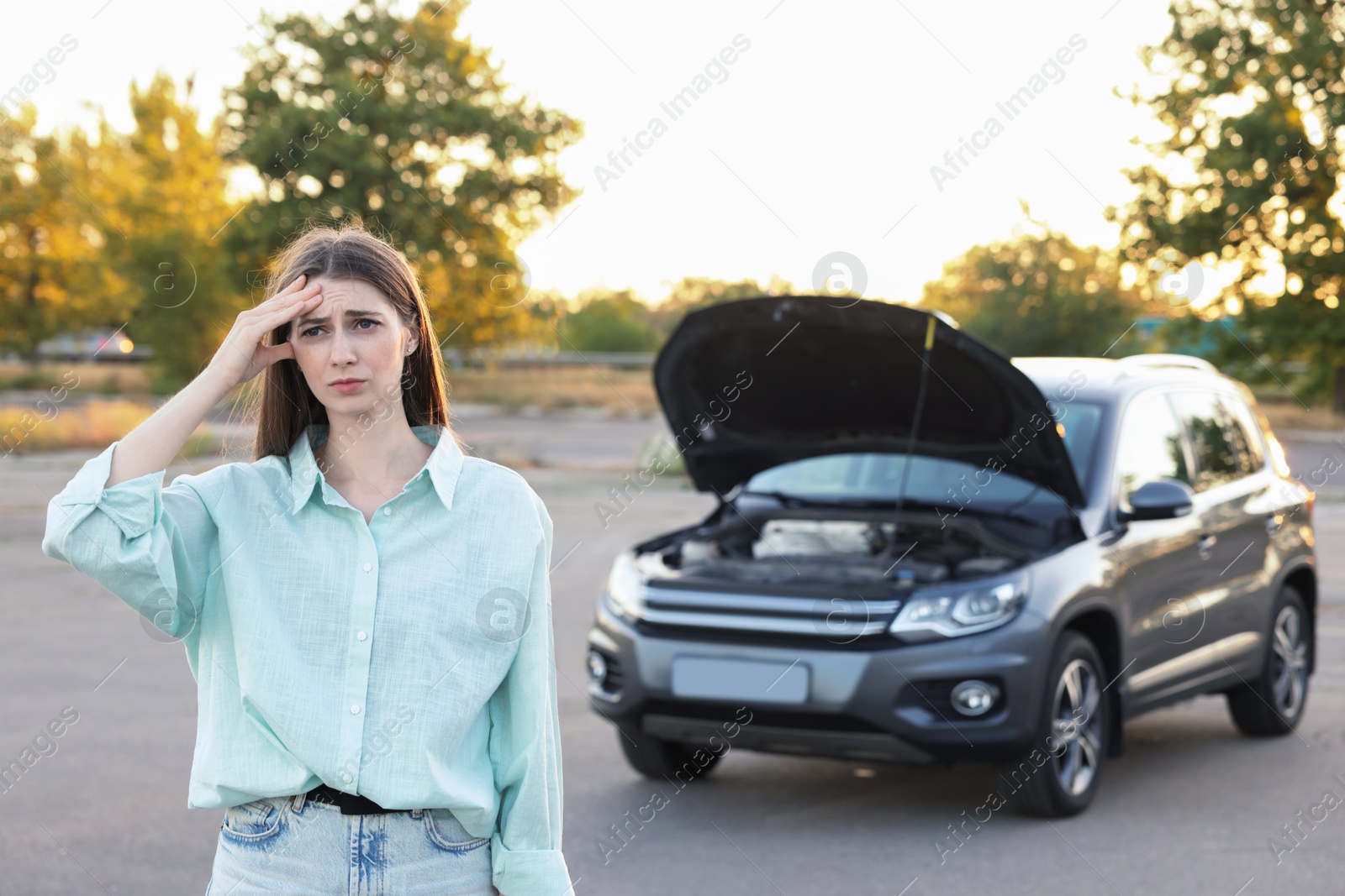 Photo of Stressed woman standing near broken car outdoors