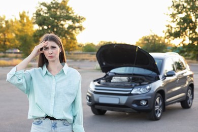 Stressed woman standing near broken car outdoors