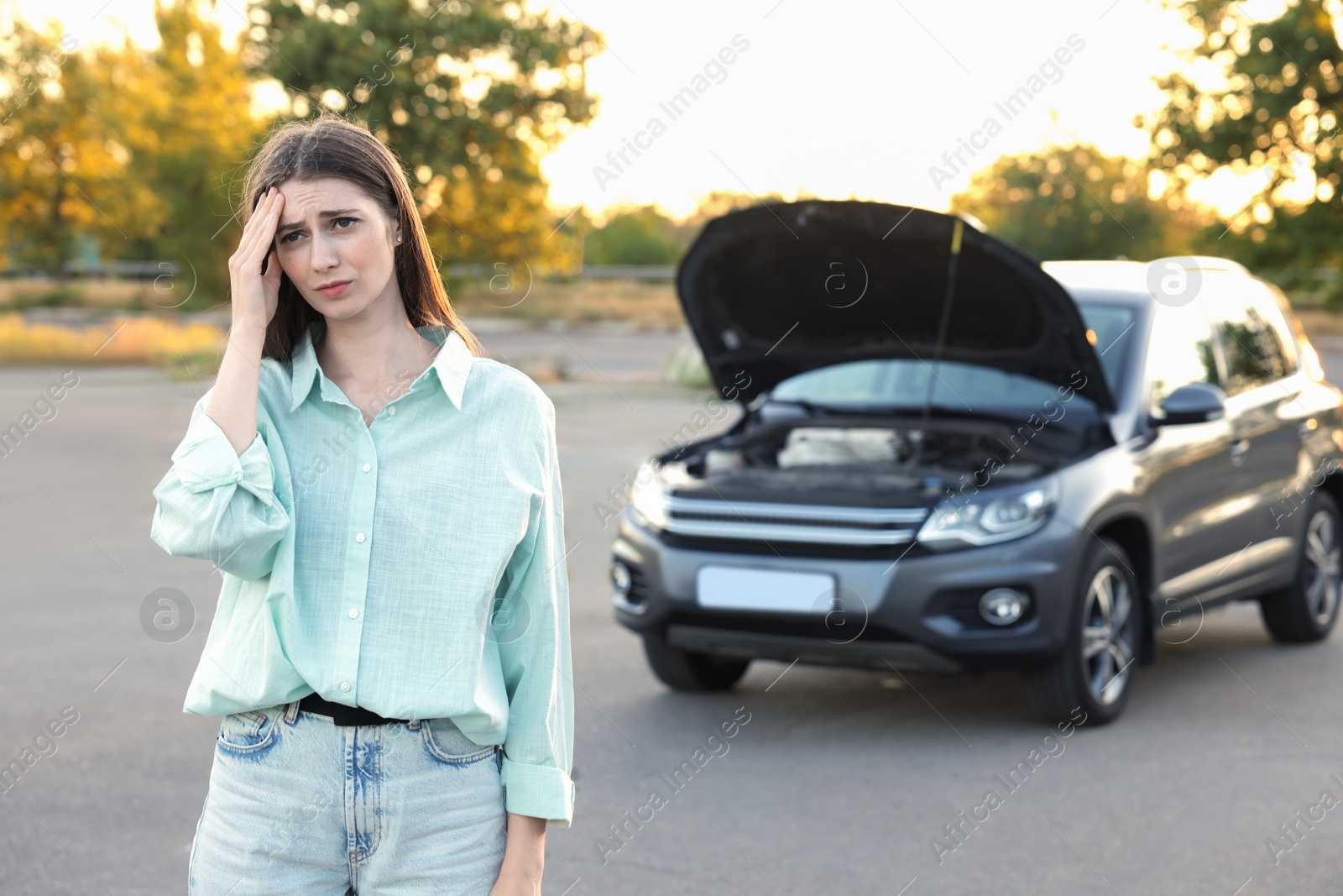 Photo of Stressed woman standing near broken car outdoors