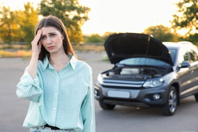 Photo of Stressed woman standing near broken car outdoors