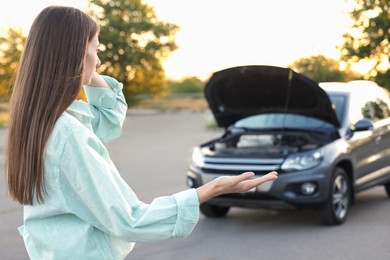 Photo of Stressed woman standing near broken car outdoors