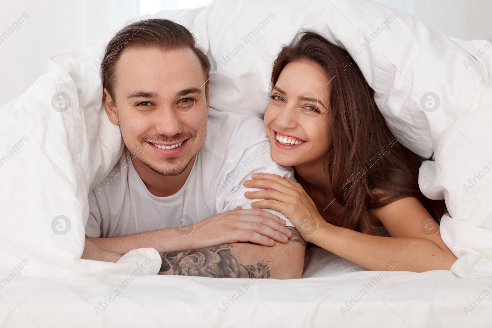 Photo of Happy couple spending time together wrapping in duvet in bed at home