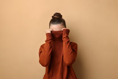 Photo of Scared young woman hiding on beige background